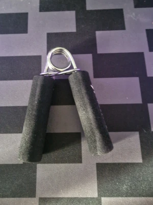 Handtränare med svarta handtag - Handtränare med svarta skumgummihandtag och metallfjäder. Perfekt för att träna greppstyrka och underarmar. Kompakt och enkel att ta med sig i väskan eller ha på skrivbordet. Passar för både träning och avkoppling.