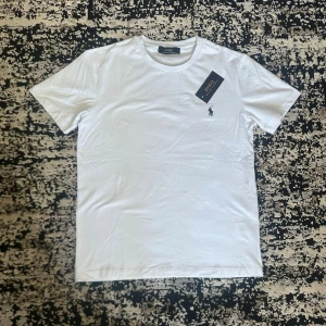 Vit t-shirt - S - Klassisk vit t-shirt med liten broderad logga på bröstet. T-shirten har rund halsringning och korta ärmar, perfekt för en clean och stilren look.