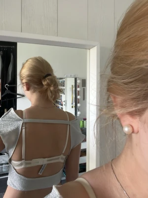 Glittrig silver croppad topp - Säljer en glittrig silverfärgad croppad topp med offshoulder-design och öppen rygg. Toppen har korta ärmar och en snygg, modern passform som verkligen sticker ut. Perfekt för dig som vill ha något extra till outfiten.