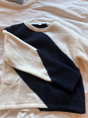 Svartvit stickad tröja  - Säljer en stickad tröja i svart och vitt med en cool diagonal färgblock-design. Tröjan har rund halsringning och långa ärmar. Materialet känns mjukt och fluffigt, perfekt för kyliga dagar. Passar dig som gillar en stilren men ändå unik look.