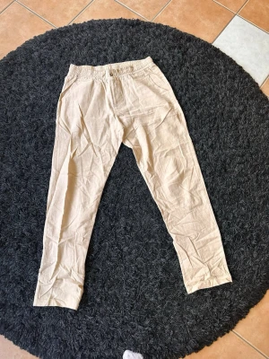 Beiga linnebyxor med resårmidja - Snygga och luftiga beiga linnebyxor med resår i midjan och raka ben. Perfekta för en avslappnad och stilren look. Gjorda i ett lätt och svalt linnematerial som passar bra till varmare dagar.