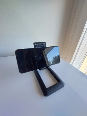 Vikbart mobiltelefonställ - Detta är ett vikbart mobiltelefonställ. Det är utformat för att hålla en mobiltelefon i antingen liggande eller stående läge. Stället kan fällas ihop för enkel förvaring och transport.