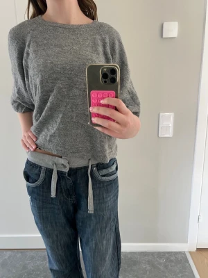 Grå stickad tröja med 3/4-ärm - Mysig grå stickad tröja med 3/4-ärm och rund halsringning. Tröjan har en avslappnad passform och är perfekt för lager på lager. Materialet ser ut att vara mjukt och bekvämt, troligen bomull eller ullblandning.