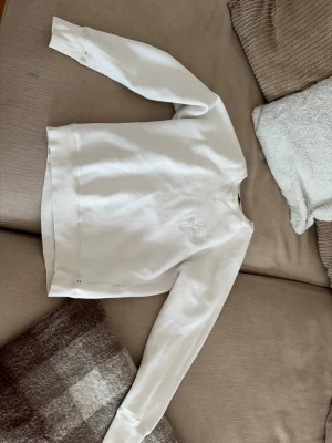Vit sweatshirt från Pelle P - Säljer en stilren vit sweatshirt från Pelle p med diskret broderad logga på bröstet. Tröjan har rund halsringning och långa ärmar. Perfekt för dig som gillar minimalistisk och clean stil.