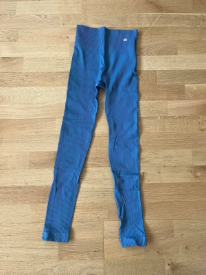 Blå ribbade tights från DOM - Blå sporttights från Drop of Mindfulness med ribbad struktur. Tillverkade i 96% polyamid och 4% elastan för maximal stretch och komfort. Hög midja och diskret logga framtill. Perfekta för träning eller chill dagar.