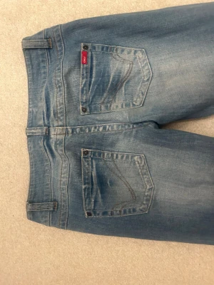 Blå jeans från ONLY med slitningar - Säljer ett par klassiska blå jeans från ONLY med snygga slitningar och tvättade detaljer. Jeansen har fem fickor, bälteshällor och knappgylf. Perfekt passform och cool vintagekänsla. Passar dig som gillar en avslappnad och trendig stil.