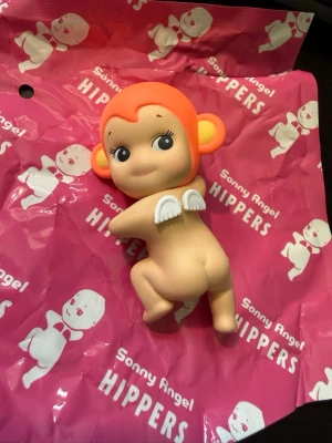 Sonny Angel Hippers figur apa - Söt samlarfigur från Sonny Angel Hippers-serien, föreställande en apa med orange huvud och öron, vita vingar på ryggen och gulligt ansikte. Tillverkad i plast och perfekt som dekoration eller samlarobjekt. Äkta från Looking Back serien