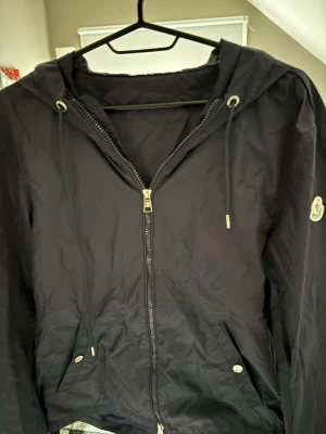 Blå vindjacka Moncler - Snygg marin blå vindjacka från Moncler med dragkedja, huva med dragsko och två fickor. Pris kan sänkas vid snabb affär. Äktenhets bevis kan ej garanteras. Jackan har en väldigt liten skada på insidan av jackan som visas på sista bilden🙌