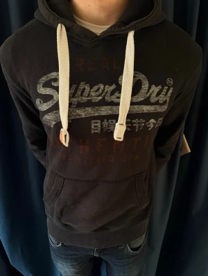 Superdry hoodie - Superdry Hoodie – Stilren & efterfrågad   Säljer en riktigt snygg Superdry hoodie i svart med klassiskt vintage-tryck. Perfekt hoodie som funkar till allt – skola, vardag eller en avslappnad look. Bekväm, stilren och lätt att matcha med jeans eller mjukis.  Märke: Superdry Färg: Svart med vitt tryck Skick: Bra använt skick Passform: Bekväm & snygg fit  En populär modell som går snabbt — först till kvarn! 🚀 Skriv vid intresse eller frågor, kan även skicka fler bilder 📩