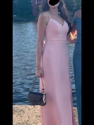 Ljusrosa långklänning med slits - Elegant ljusrosa långklänning med smala axelband och v-ringad urringning. Klänningen har en stilren passform och en diskret slits framtill som ger en snygg detalj. Perfekt för sommarens speciella tillfällen såsom bal eller fest. Endast använt 1 gång och är därmed i nyskick. Nypris: 1599kr Mitt pris:1099