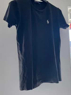 Svart t-shirt från Polo Ralph Lauren - Svart t-shirt från Polo Ralph Lauren med klassisk rund hals och korta ärmar. Diskret logga broderad på bröstet i vitt.