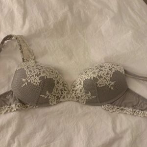 Grå bh med spetsdetaljer - Snygg grå bh med vacker vit spets över kuporna och axelbanden. Den har en elegant design som passar perfekt under alla kläder. Justerbara axelband för bästa passform. Från Intimissimi i storlek 75b! 