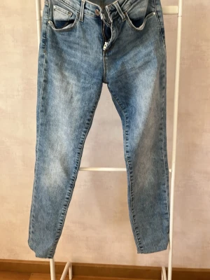 Ljusblå raka jeans från Guess - Säljer ett par ljusblå jeans från Guess med klassisk femficksmodell och raka ben. Jeansen har normal midja, bälteshällor och dragkedjegylf. Materialet är denim i bomull och bakfickan har Guess-loggan. Perfekta för en avslappnad och trendig look.
