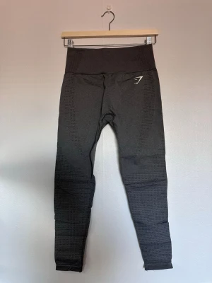 Mörkgrå seamless leggings Gymshark - Säljer ett par mörkgrå seamless leggings från Gymshark med hög midja och diskret mönster längs benen. Stretchigt material som sitter tight och bekvämt. Gymshark-logga på höften och vristen. Perfekta för träning eller chill.