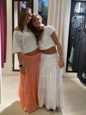 Vit långkjol med volangdetaljer - Säljer en vit långkjol med flera volangdetaljer och resår i midjan. Kjolen har en luftig och flowy känsla, perfekt för varma dagar. 