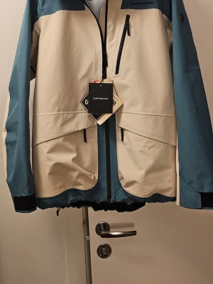 Peak Performance vindjacka blå/beige - Peak Performance – Ny jacka med tagg!   Säljer en helt ny, oanvänd Peak Performance‑jacka i en omsnygg tvåfärgad design (beige + blå). Jackan är lätt, sportig och perfekt för vår, höst och mildare vinterdagar. Kvalitet rakt igenom – och självklart äkta, med taggar kvar. 