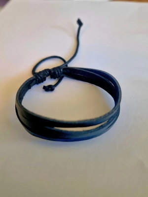 Svart läderarmband med justerbar knut - Snyggt svart armband i läder med flera tunna remmar och justerbar knut. Perfekt accessoar för en stilren och avslappnad look. Passar både tjejer och killar som gillar minimalistiska smycken.