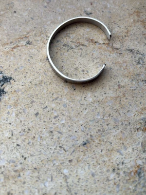 Silvrigt stelt armband i metall - Snyggt stelt armband i silverfärgad metall med minimalistisk och stilren design. Armbandet är öppet och har en slät, blank yta som ger en modern känsla. Perfekt accessoar för att lyfta din outfit.