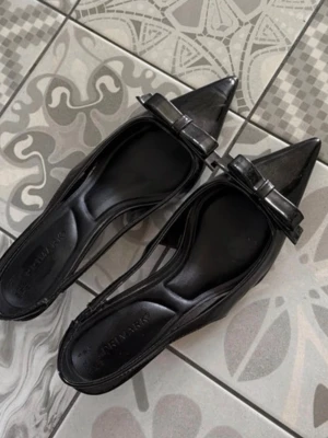 Svarta pumps med rosett från Primark - Stilrena svarta pumps från Primark med spetsig tå och dekorativ rosett framtill. Skorna har en låg klack och är tillverkade i ett glansigt material som ger en elegant look. Perfekta för dig som gillar klassiska detaljer och vill ha en feminin touch.