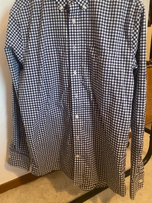 Gant Blårutig skjorta från Levi's - Säljer en klassisk Gant blårutig skjorta med vit bas och knappar framtill. Skjortan har lång ärm, bröstficka och button-down krage. Perfekt för dig som gillar tidlös stil och rutigt mönster.