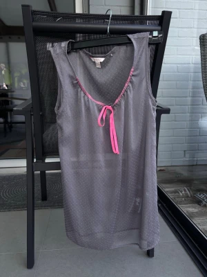 Grått linne med rosa detaljer Esprit - Snyggt och luftigt linne från Esprit i grått med små vita prickar. Ärmlös modell med djup ringning och rosa band vid halsen som knyts framtill. 