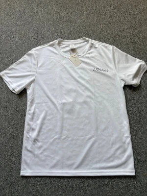 Vit t-shirt från LTHwear - (PRIS:249kr kan gå ner till max 239kr) Snygg vit t-shirt från LTHwear med diskret logga på bröstet. T-shirten har rund hals och korta ärmar, perfekt för dig som gillar en clean och enkel stil. Materialet är polyester vilket gör den lätt och bekväm att bära.