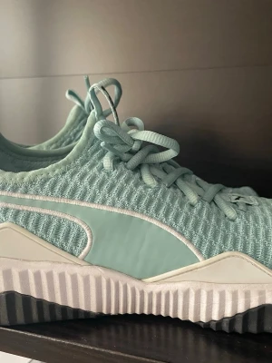 Mintgröna sneakers från Puma - Snygga mintgröna sneakers från Puma med stickad ovandel och tydliga vita detaljer. Skorna har en chunky, räfflad sula och klassisk snörning. Perfekta för dig som gillar sportig och modern stil. Puma-logga syns tydligt på hälen.