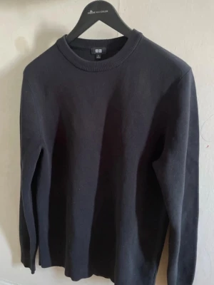 Svart  tröja från Uniqlo, storlek M - En stilren svart tröja från Uniqlo i storlek M. Tröjan har rund halsringning, långa ärmar och är tillverkad i ett mjukt material som passar perfekt till olika outfits. Enkel och klassisk design utan mönster.