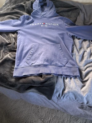 Lila hoodie från Tommy Hilfiger - Snygg lila hoodie från Tommy Hilfiger med klassisk logga broderad på bröstet. Hoodien har en stor magficka och ribbade muddar vid ärmslut och nederkant. Perfekt för en avslappnad och trendig look.