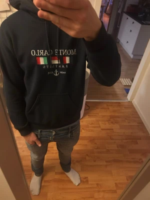 Mörkblå Monte Carlo hoodie - Snygg mörkblå hoodie från Monte Carlo med tryck framtill i vitt, grönt och rött samt texten 'Yacht Club'. Klassisk känguruficka och justerbar huva med snören. Perfekt för dig som gillar stilrena och bekväma plagg med en touch av marina vibbar.