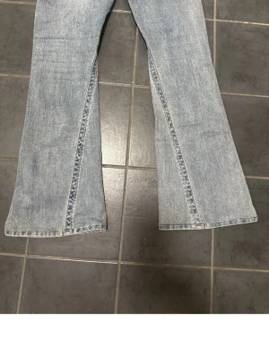 Ljusblå utsvängda jeans - Säljer ett par ljusblå jeans med utsvängda ben och markerade sömmar framtill. Jeansen har en klassisk femficksmodell och är tillverkade i denim. Perfekta för en trendig och avslappnad stil.