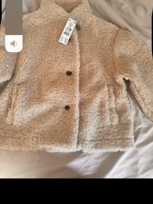 Pile jacket light beige  - Mysig beige teddyjacka från Gina tricot med två knappar framtill och två sidofickor. Jackan har en boxy passform och är gjord i fluffigt teddy-material som ger en trendig look. 
