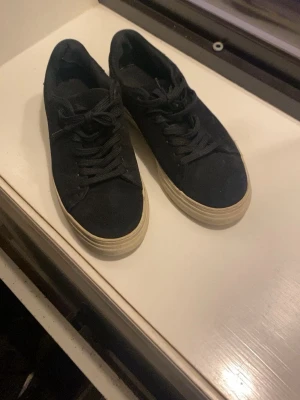 Svarta sneakers från Selected Homme - Stilrena svarta sneakers från Selected Homme med lågt skaft och vit sula. Skorna har klassisk snörning och ovandel i tyg som ger en clean look. Perfekta för dig som gillar minimalistisk stil och vill ha ett par enkla men snygga sneakers. Varför jag säljer dessa så billigt är för skadan i hälen som inte känns i foten, och för att jag fick dessa väldigt billigt av en kompis (nypris ca 1200kr)