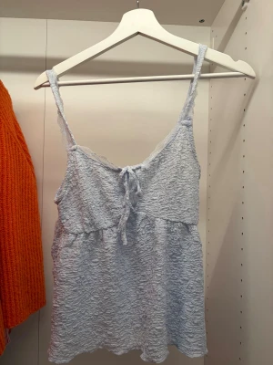 Ljusblå spetslinnetopp Gina Tricot - Supersöt ljusblå linnetopp från Gina Tricot med spetsdetaljer och knyt framtill. Toppen har tunna axelband och är tillverkad i ett mjukt, spetsliknande material som ger en romantisk vibe. Perfekt att styla med jeans eller kjol för en fräsch look.