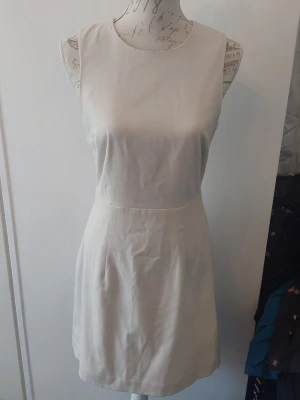 Vit ärmlös kortklänning - Stilren vit kortklänning med rund halsringning och ärmlös design. Klänningen har en figurnära passform och dragkedja i ryggen för enkel påklädning. Perfekt för dig som gillar minimalistisk och klassisk stil.