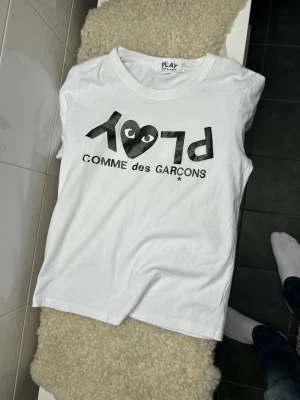 Vit Comme des Garçons PLAY t-shirt - Säljer en galet fet vit t-shirt från Comme des Garçons PLAY med det ikoniska hjärtmotivet och svart text på bröstet.  Säljer den för att den är för liten för mig. Väldigt bra skick förutom en liten defekt som knappt syns på bokstaven C. Nypris ligger runt 1200kr 