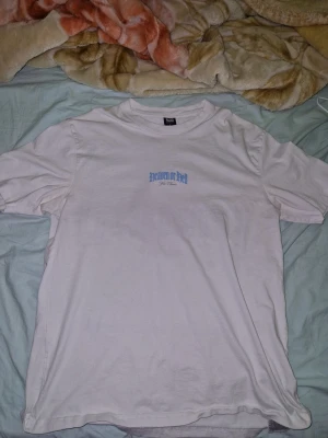 Vit t-shirt från Black Squad - Vit t-shirt från Black Squad med relaxed fit och trycket 'Heaven or Hell' i ljusblått framtill. Klassisk rund halsringning och korta ärmar. Tillverkad i mjuk bomull, perfekt för en chill och enkel stil.