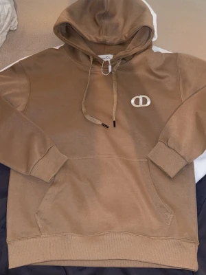 D*or Beige hoodie ny - Snygg beige hoodie från D*or med klassisk huva och dragsnören. Hoodien har en stor magficka och ribbade muddar vid ärmar och nederkant. Perfekt för en avslappnad och trendig look.