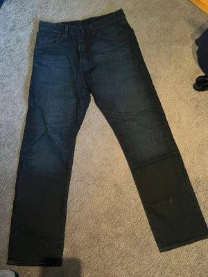 Mörkblå raka jeans från Levi's - Snygga mörkblå jeans från Levi's med klassisk rak passform och fem fickor. Jeansen har en diskret tvätt och är tillverkade i slitstark denim. Perfekta för dig som gillar en tidlös och enkel stil. Levi's-logga på bakfickan och patch bak i midjan. Använda 1 gång