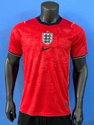 England röd matchtröja Nike - Snygg röd England matchtröja från Nike med svart krage och vita detaljer. Tröjan har det engelska landslagets emblem på bröstet och ett diskret mönster i tyget. Perfekt för fotbollsfans som vill sticka ut på läktaren eller planen.
