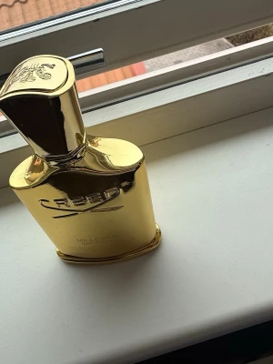Creed Millésime Impérial 100ml - Lyxig parfymflaska från Creed i modellen Millésime Impérial. Flaskan är i glänsande guld med elegant, rektangulär form och rundade kanter. Märkets logga och namn är präglade på framsidan. Rymmer 100 ml och ger en exklusiv känsla i badrumshyllan.
