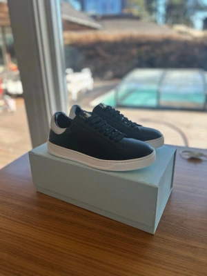OANVÄNDA Lanvin Herrskor 44 Svart - Snygga sneakers från Lanvin i svart läder med vita detaljer, perfekta inför våren. Skorna har aldrig haft en fot i sig, aldrig klivit ett steg, sprillans nya som ni kan se på den andra bilden. De är självklart äkta och kvitto ingår. Antingen kan ni hämta dem i sollentuna eller så kan jag frakta de med köparskydd. Storleken är 44, är något större i passform. nypris ligger på 5000kr, mitt pris endast 2699kr.