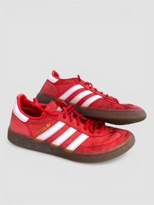 Adidas Spezial röda sneakers - Röda Adidas Spezial sneakers med klassiska vita ränder på sidorna och guldfärgad logga. Ovandelen är i mocka och textil, med bruna gummisulor och röda skosnören. Låg modell med retrovibbar och tydliga detaljer i vitt på häl och plös.