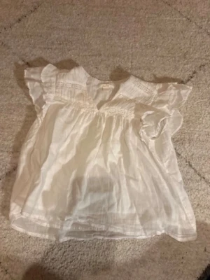 Vit blus med volangärmar - Söt vit blus med volangdetaljer vid ärmarna och smock upptill. Blusen har en luftig passform och är tillverkad i ett tunt, lätt tyg som passar perfekt till varmare dagar. Enkel att styla med både jeans och kjol.