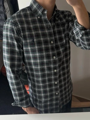 Rutig skjorta från Polo Ralph Lauren - Säljer en klassisk långärmad skjorta från Polo Ralph Lauren med rutigt mönster i mörkblått, grönt och vitt. Skjortan har knappar hela vägen och button-down krage. Perfekt för dig som gillar en tidlös och snygg stil.