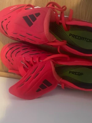 Adidas Predator pro  röda fotbollsskor - Säljer ett par röda Adidas Predator fotbollsskor med svarta och vita detaljer. Skorna har en modern design med mönstrade ovandel och plastdobbar för bra grepp på planen. Perfekta för dig som vill ha stil och kontroll på matchen. Ny pris runt 1000kr och köptes för 1200(när de va nya) endast använd ca 8 träningar och är i mycket bra skick 