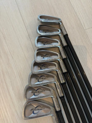Golfklubbor PureSpin set - Säljer ett set med PureSpin Diamond Face Scoring Iron golfklubbor. Klubborna har silverfärgade huvuden och svarta skaft med svarta grepp och gulddetaljer. Perfekt för dig som vill ta ditt golfspel till nästa nivå.