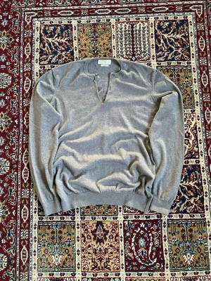 Grå stickad tröja The Tailoring Club - Säljer en stilren grå stickad tröja från The Tailoring Club i storlek XL. Fits like M Tröjan har två knappar vid halsen och ribbade muddar vid ärmslut och nederkant. Perfekt för dig som gillar en enkel men snygg look.