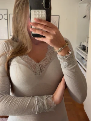Intemissimi spetstopp  - Supersnygg ljusgrå långärmad topp med v-ringning och fina spetsdetaljer vid halsringning och ärmslut. Mjuk och stretchig känsla, perfekt för en chill och stilren look. Ingen synlig logga eller märke.
