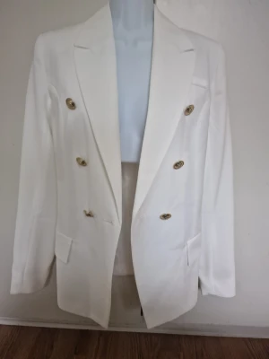 Vit dubbelknäppt kavaj med guldknappar - Stilren vit kavaj med dubbelknäppning, den är helfodrad och har en figurnära passform som framhäver silhuetten. Snygg för både formella tillfällen och för att lyfta en outfit 🤍